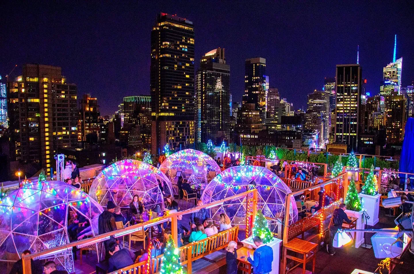 Night view of 230 Fifth Rooftop in New York City with lit igloos and city skyline.
