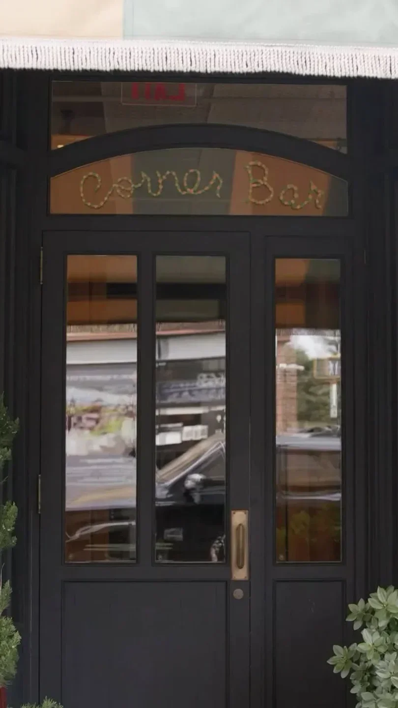Entrance of Corner Bar in New York City with the restaurant's name on the glass door.
