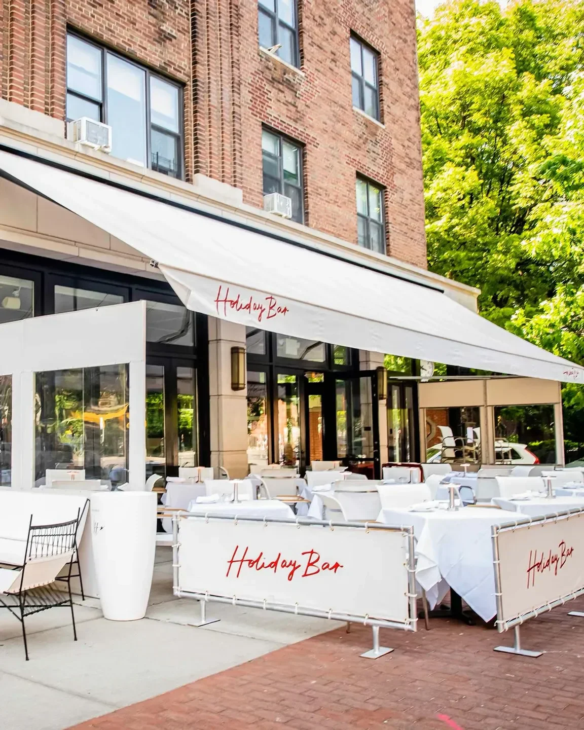 Outdoor seating at Holiday Bar in New York City with white tables and awnings.