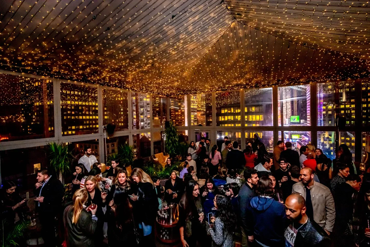Lively crowd at PHD Midtown rooftop bar in New York City under starry string lights